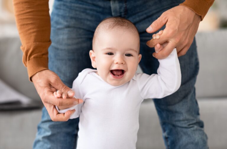 Kiedy pierwsze zęby - radosne niemowlę trzymające się rąk dorosłego, przygotowując się do pokazania pierwszych zębów