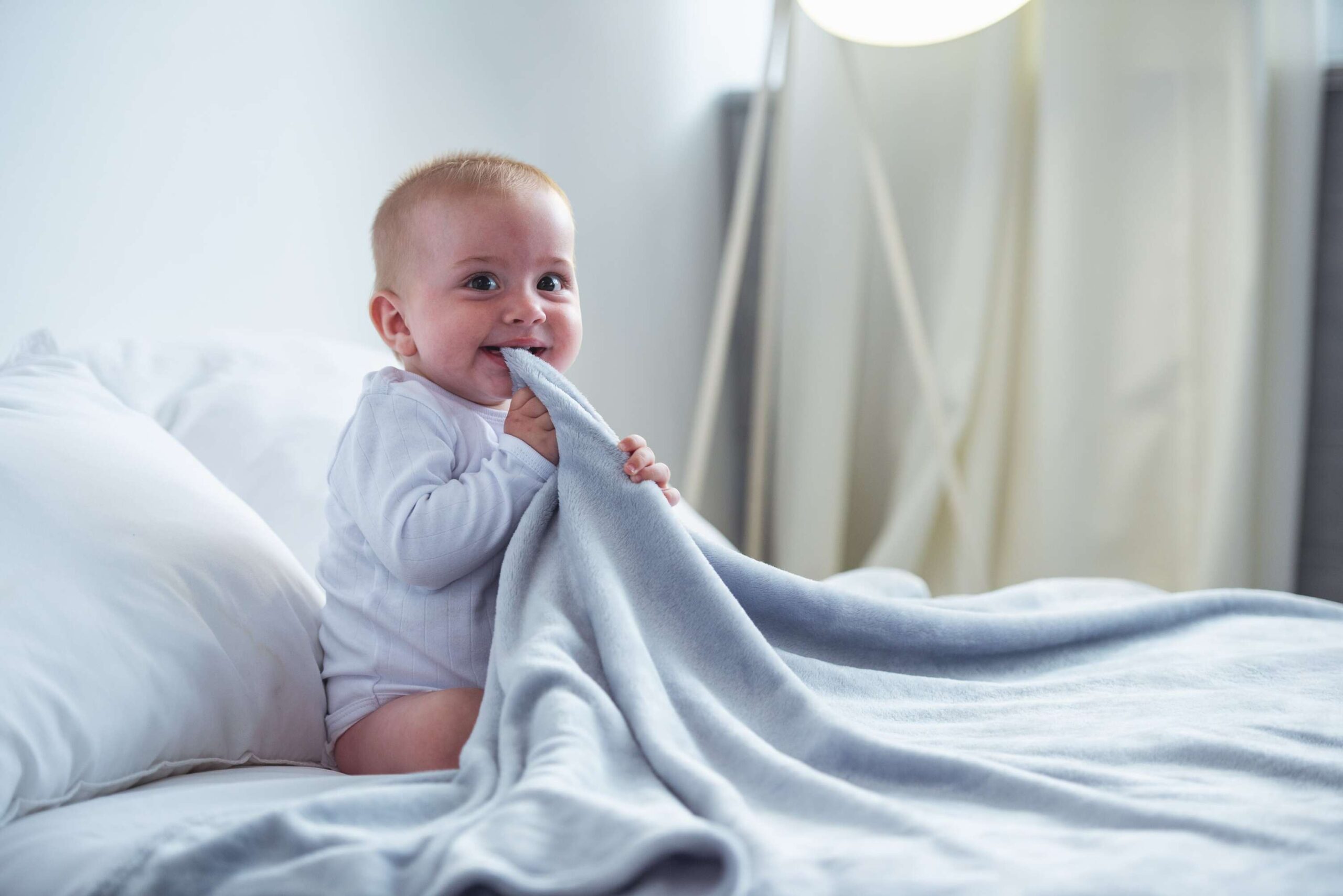Ząbkowanie - uśmiechnięte niemowlę gryzące koc podczas ząbkowania, ważny etap w rozwoju dziecka